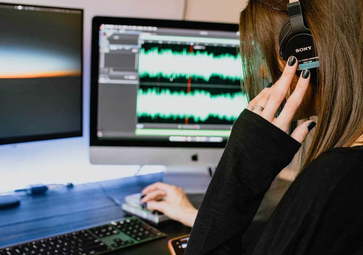 woman with her left hand raised to the headphones she is wearing while her right hand adjusts sound balance on the music for marketing videos she is editing