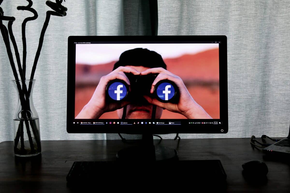 Computer screen showing man with binoculars on his eyes. The ends of the binoculars display the Facebook logo.