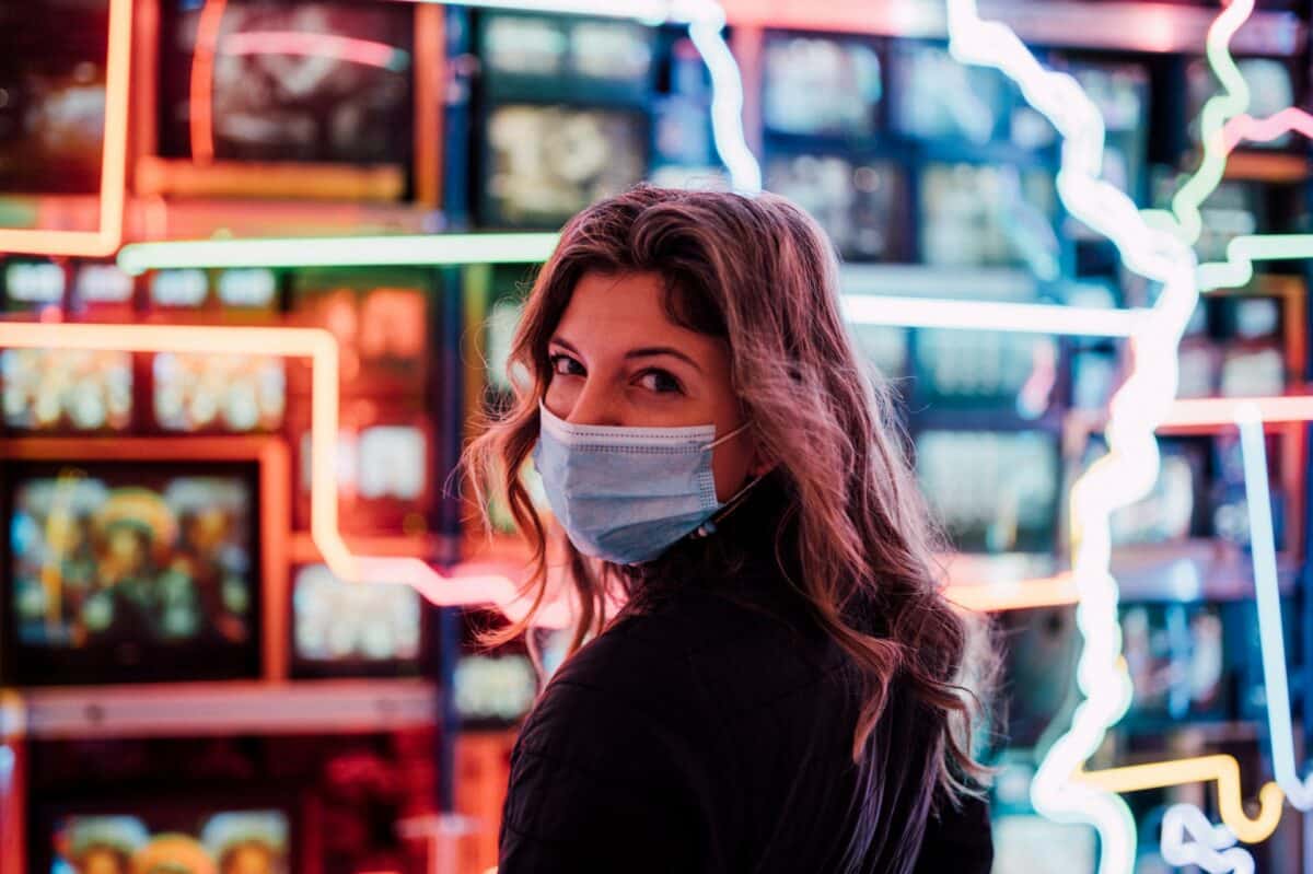 woman wearing a face mask standing in front of a wall of television screens
